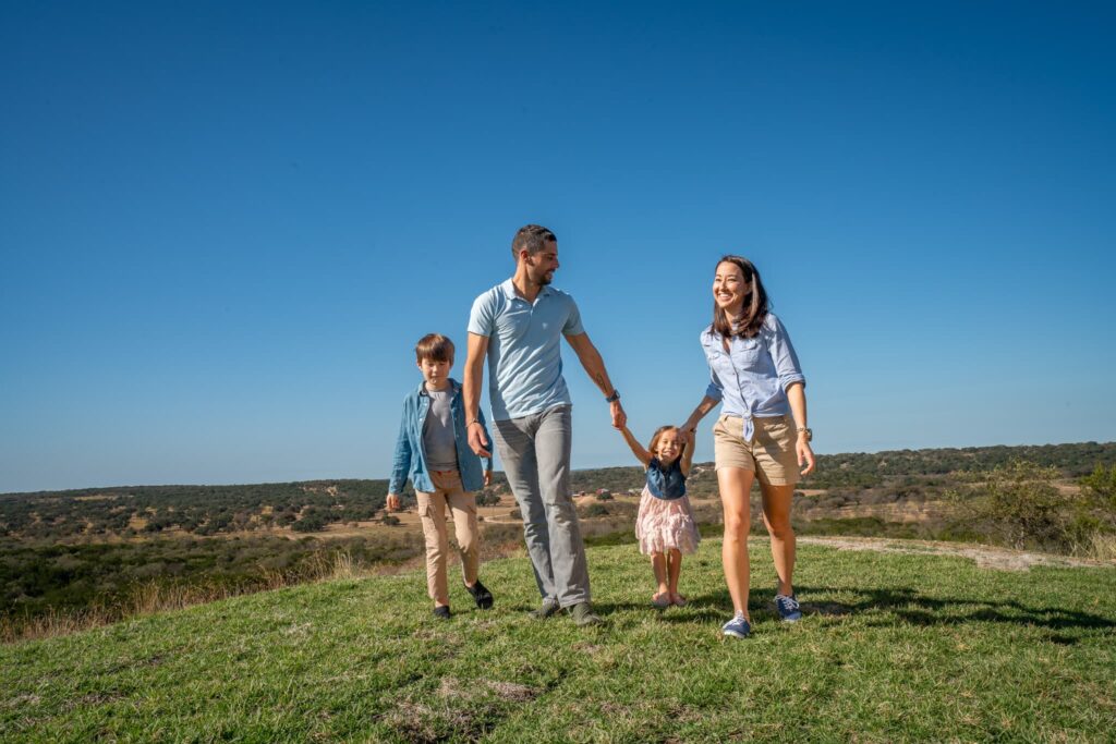 A family of four hiking with the children hilltop at Artemis Ranch enjoying Hill Country views and ranch adventures
