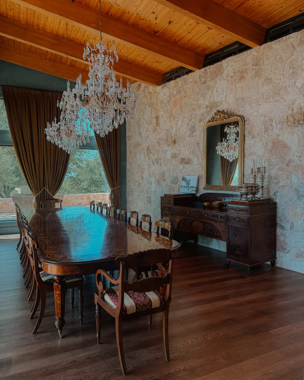 Inside Artemis Lodge - dining room with long wooden table, chandeliers and stone wall